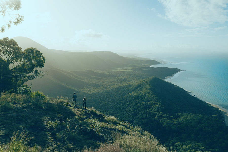 Two people are standing on top of a mountain, looking out to the ocean