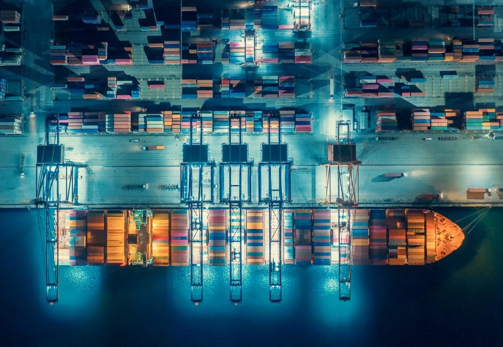 Aerial photo of a busy port lit up at night. A container ship is being loaded.