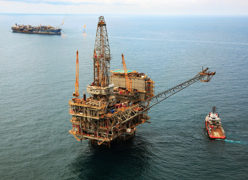 Aerial photo of a large oil rig and support boat, with an FPSO in the background